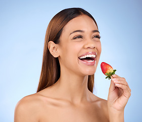 Image showing Skincare, wellness and woman with a strawberry in studio with a healthy, natural and face routine. Happy, beauty and female model with dermatology facial treatment eating red fruit by blue background