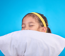 Image showing Little girl, pillow and sleep in a studio feeling tired, fatigue and ready for dreaming. Isolated, blue background and happy young child with pillows and closed eyes for sleeping, rest and nap