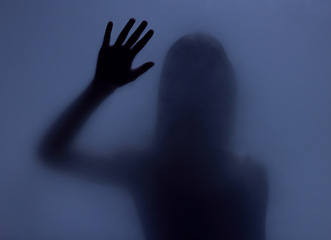 Image showing Shadow, glass and hand with a woman in studio on a blue background for mystery or sensual secrecy. Creative, silhouette and window with a female posing for beauty, art deco or feminine desire