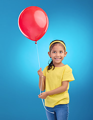 Image showing Happy girl, studio and red balloon of a an excited kid with a smile ready for a birthday party. Celebration, happiness and young child holding balloons in the air with isolated blue background