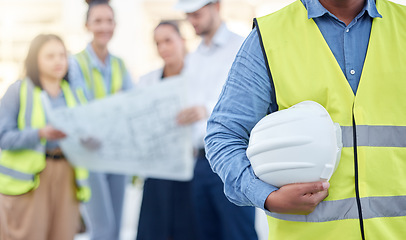 Image showing Helmet, construction and an architect standing on a building site with his team planning in the background. Leadership, architecture and renovation with an engineer holding a hard hat for maintenance