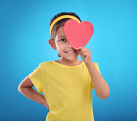 Image showing Portrait, heart cut out and girl with smile, joyful and cheerful against blue studio background. Face, female kid and young person with symbol for love, happiness and joyful with development and sign