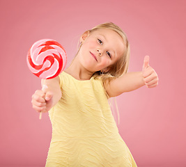 Image showing Candy, thumbs up and lollipop with portrait of girl in studio for sugar, party and carnival food isolated on pink background. Cute, positive and youth with child or eating snack for playful and treat