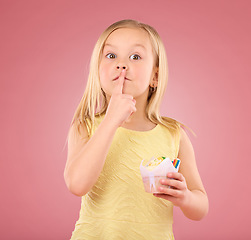 Image showing Girl child, finger on lips and cupcake portrait in studio on a pink background for hush and silence. Face of female kid model with cake, secret and sweet snack in hand isolated on color and space