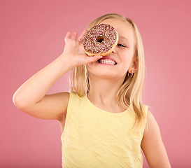 Image showing Child, donut and smile portrait in studio on a pink background while happy about sweet snack. Girl kid model with happiness, creativity and chocolate ring over eye in hand isolated on color and space