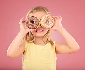 Image showing Child, donut over eyes and smile in studio with sweet snack in hands on a pink background. Girl kid model with happiness, creativity and comic face holding food in hand isolated on color and space