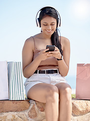 Image showing Woman relax after shopping, smartphone and headphones, listening to music outdoor with retail therapy and rest. Happy female, paper bag and communication with chat on social media app and technology