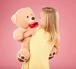 Image showing Teddy bear, happy and back of a child in studio with a big, fluffy and cute toy as gift or present. Adorable, innocent and young girl kid hugging her teddy with care and happiness by pink background.