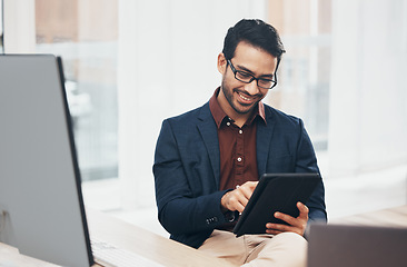 Image showing Office, happy Indian man at desk with tablet and computer, reading good news email or successful sales report online. Business, smile and communication with internet, social media or research on web.