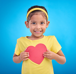 Image showing Portrait, smile and girl with heart cutout, joy and cheerful against a blue studio background. Face, Indian female child and kid with love symbol, excited and young person with sign, mockup and happy