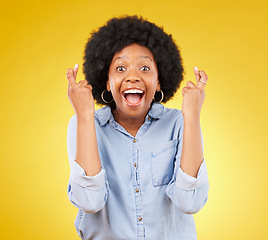 Image showing Happy, portrait and fingers crossed by black woman in studio for wish, hope and good luck against yellow background. Face, hands and emoji by excited female with wow, surprised and hopeful gesture