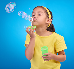 Image showing Children, blue background and a girl blowing bubbles in studio for fun or child development of motor skills. Kids, game or soap and a cute or adorable female child playing with a bubble wand