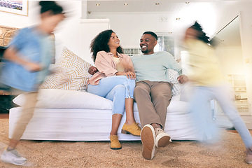 Image showing Children running, happy home and couple on a sofa, talking and relax while bonding in a living room. Blur, kids and content parents on a couch, smile and enjoying weekend indoors with playing and fun