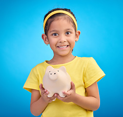 Image showing Face portrait, piggy bank and girl child in studio isolated on a blue background. Happy, smile and kid with cash box, savings or financial, investment or learning budget, finance growth or money.