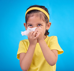 Image showing Sick, blowing nose and napkin with girl in studio for allergies, illness and sneezing. Hay fever, bacteria and sinus issue with child and tissue isolated on blue background for health, medical or flu