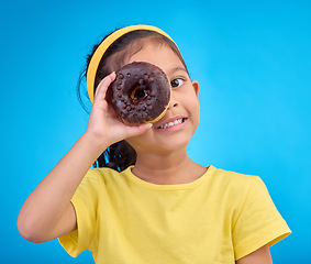 Image showing Donut, eye and smile with portrait of girl in studio for junk food, sugar and happiness. Snack, cake and cute with face of child and dessert for cute, positive and chocolate on blue background