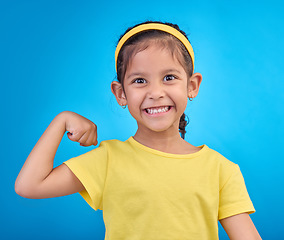 Image showing Strong, happy and portrait of a child with muscle isolated on a blue background in a studio. Excited, smile and girl kid showing biceps, arms and power from exercise with confidence on a backdrop