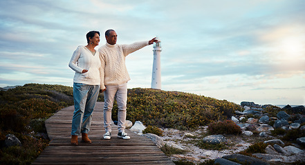 Image showing Travel, love and elderly couple pointing on boardwalk at beach, calm at a lighthouse against sunset sky. Senior, man with woman on ocean trip, holiday or vacation, happy and enjoying retirement