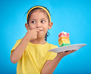 Image showing Birthday cake, taste and young girl with a sweet in studio eating icing for party event dessert. Celebration, rainbow food and hungry kid in a isolated and blue background studio ready to celebrate