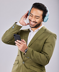 Image showing Asian man, phone and smile listening to music on headphones against a gray studio background. Happy formal male smiling on smartphone with headset for audio streaming or entertainment on mobile app