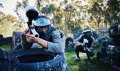 Image showing Team, paintball and tires for cover, hiding or protection while firing or aiming down sights together in nature. Group of paintballers waiting in teamwork for opportunity to attack or shoot in sports