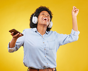 Image showing Phone, music headphones and black woman singing in studio isolated on a yellow background. Dance, cellphone and happy female with mobile for streaming, dancing and enjoying radio, podcast or audio.