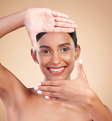 Image showing Portrait, hands and frame with a model woman in studio on beige background for beauty or skincare. Face, skin and hand gesture with an attractive young female posing for cosmetics or luxury wellness