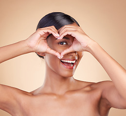 Image showing Portrait, heart and hand gesture with a woman in studio on a beige background for beauty or skincare. Face, hands and emoji with an attractive young female posing for cosmetics or luxury wellness