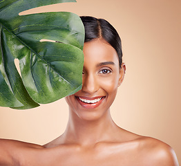 Image showing Portrait, beauty and palm leaf with a model woman in studio on a beige background for natural skincare. Face, plants and nature with an attractive young female posing for cosmetics or luxury wellness