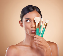 Image showing Skincare, brush and Indian woman with makeup, foundation and funny on brown studio background. Female, lady or cosmetics tools with glamour, elegant or beauty for luxury grooming or facial expression