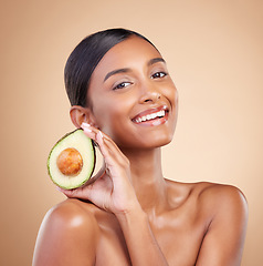 Image showing Portrait, skincare and avocado with a model woman in studio on a beige background for beauty. Face, fruit and antioxidants with an attractive young female posing for organic or natural cosmetics
