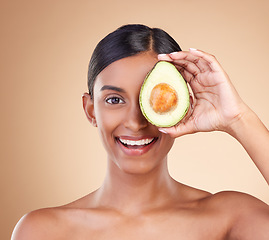 Image showing Portrait, beauty and avocado with a model woman in studio on a beige background to promote skincare. Face, eye and fruit with an attractive young female posing for organic or natural antioxidants