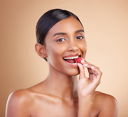 Image showing Portrait, beauty and woman biting a strawberry in studio on a beige background to promote skincare. Face, fruit and eating with an attractive young female posing for organic or natural cosmetics