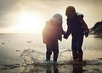Image showing Beach, sunset and silhouette of children in water splash together, holding hands and playing in waves. Fun, holiday and brothers, happy in boots on ocean vacation, jumping in sea on winter evening.