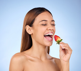 Image showing Skincare, health and female with a strawberry in studio with a wellness, natural and face routine. Happy, beauty and woman model eating red fruit for nutrition, diet and self care by blue background.