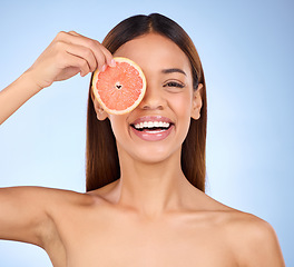 Image showing Beauty, woman and grapefruit for face portrait with a smile for skincare dermatology. Model on a blue background for self care, facial glow and healthy fruit with vitamin c for clean skin in studio