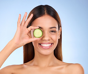 Image showing Beauty, woman and cucumber for face portrait with a smile and dermatology skincare cosmetic. Female model on blue background for self care, facial glow and vegetable for natural skin health in studio