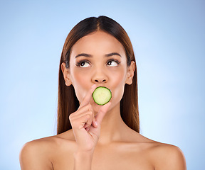 Image showing Cucumber, woman and skincare face portrait with beauty and dermatology cosmetics. Female model on a blue background thinking about self care, facial glow and healthy fruit for natural skin in studio