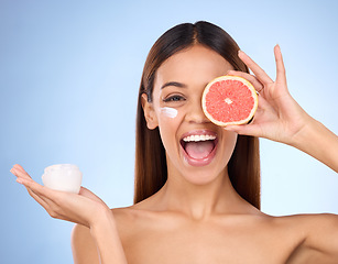 Image showing Woman, moisturizer cream and grapefruit for natural skincare beauty and vitamin C against blue studio background. Portrait of happy female holding fruit, creme or lotion for healthy organic products