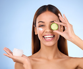 Image showing Woman, moisturizer cream and cucumber for natural skincare, beauty and cosmetics against blue studio background. Portrait of happy female holding vegetable, creme or lotion for healthy organic facial