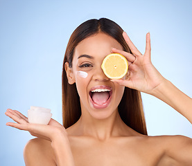 Image showing Woman, moisturizer cream and lemon for natural skincare, beauty and vitamin C against blue studio background. Portrait of happy female holding citrus fruit, creme or lotion for healthy organic facial