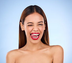 Image showing Wink, woman and red lipstick makeup portrait with cosmetics on face in studio. Aesthetic female model on a blue background for self care, facial glow and beauty or color for skin with tongue out