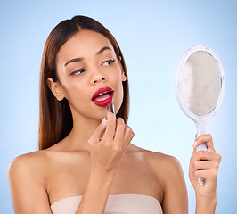 Image showing Beauty, woman and red lipstick or makeup with mirror in hand for face cosmetic product in studio. Aesthetic female model on a blue background with color application on lips for shine and self care