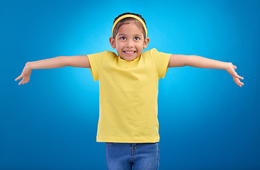 Image showing Girl, child and happy or shrugging or unsure in studio with arms and hands stretched with a smile. Kid on blue background clueless, doubt and confused about question or reaction with hand gesture