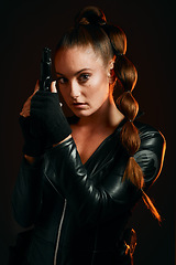 Image showing Portrait, gun and spy with a woman assassin in studio on a dark background ready for combat. Hero, leather and power with an attractive young female secret agent holding a weapon on a mission
