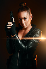 Image showing Portrait, gun and secret agent with a woman assassin in studio on a dark background ready for combat. Hero, leather and power with an attractive young female spy holding a weapon on a mission