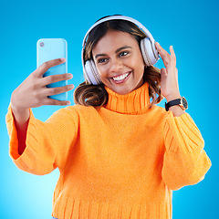 Image showing Music headphones, smile and selfie of woman in studio isolated on a blue background. Profile picture, radio and happy Indian female streaming, listening and enjoying sound, audio podcast or song.