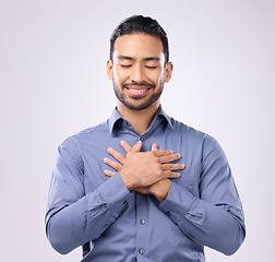 Image showing Pray, hands on chest and happy man in studio with self love, hope and love on grey background. Praying, hand and open heart gesture by male show emoji, gratitude and calm zen while standing isolated