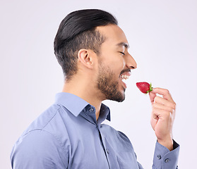 Image showing Healthy, diet and a man eating a strawberry in studio on a gray background for natural nutrition. Food, fruit and vegan with a handsome young male biting a red, juicy or tasty berry for dessert