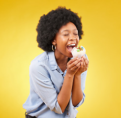 Image showing black woman, cupcake and excited or happy in studio while eating sweet food on a yellow background. African female model with snack, dessert or cake for happiness, birthday or celebration mockup